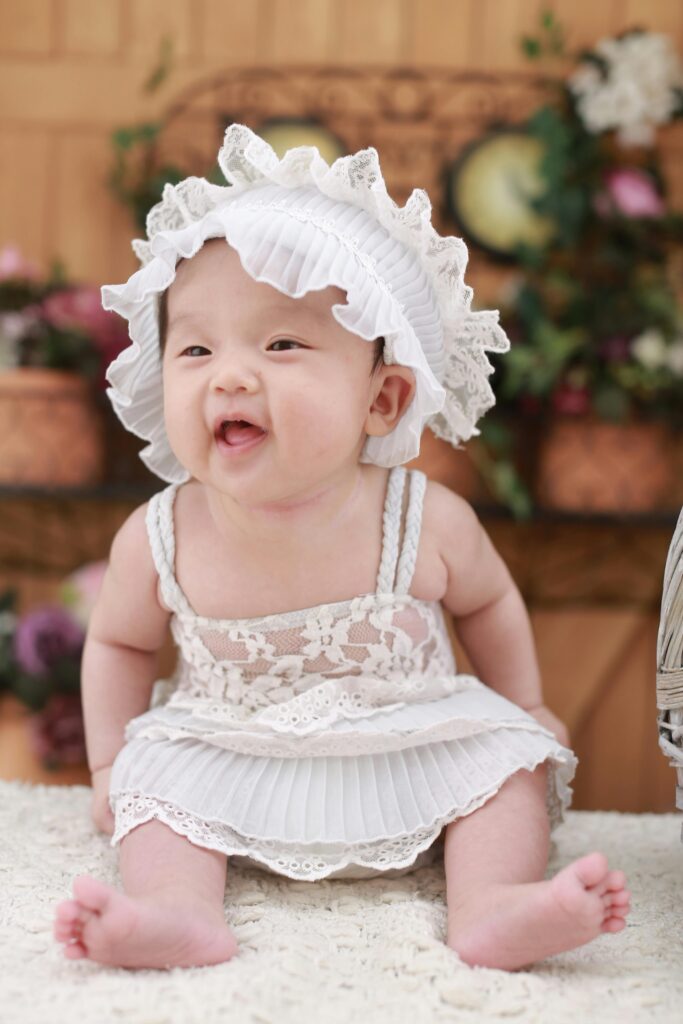 Cute baby girl wearing a lace dress and hat, smiling happily indoors.