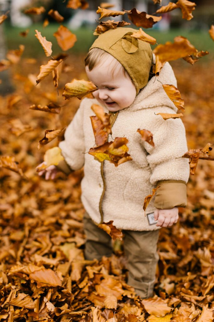 Adorable toddler enjoying a playful moment with autumn leaves outdoors.