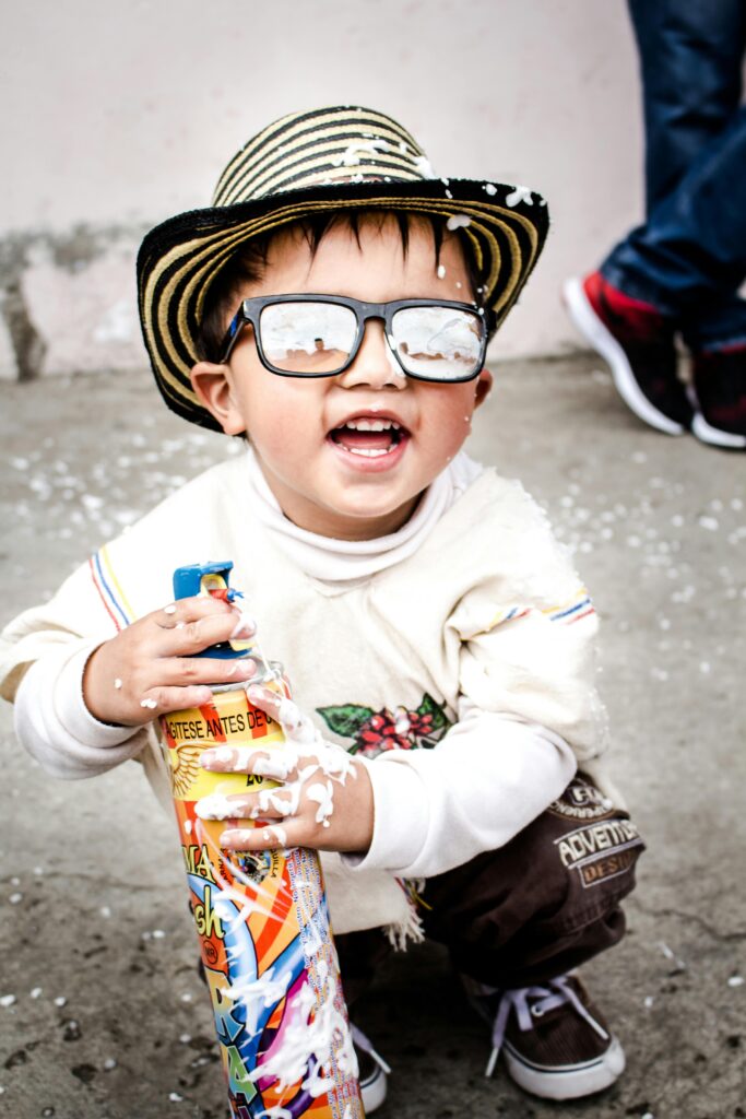 Happy child wearing sunglasses and a hat playing with foam spray in Colombia.